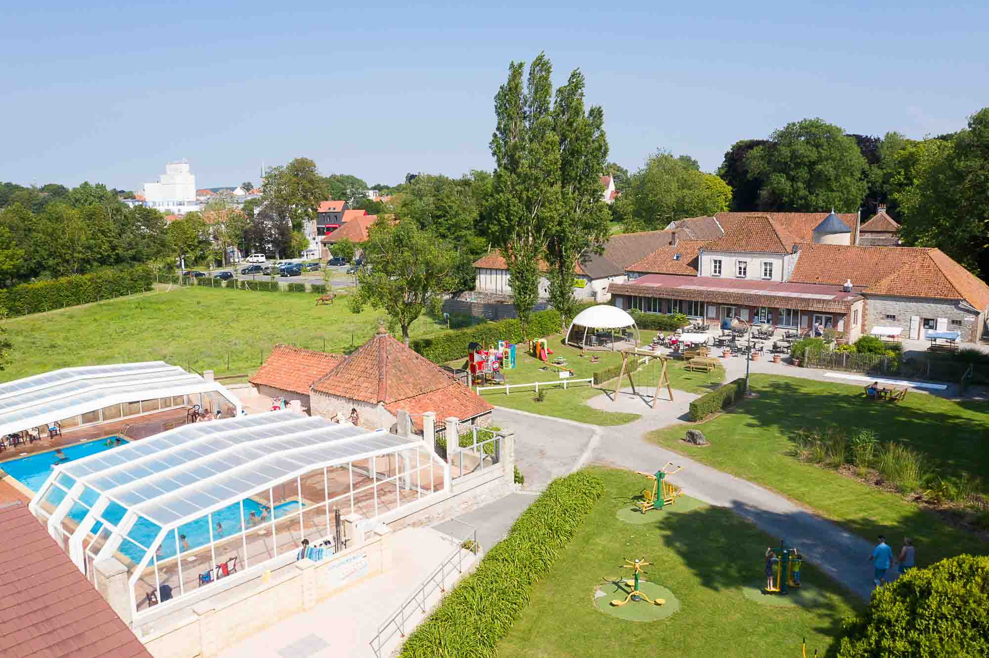 Vue aérienne du Castel Camping la Bien Assise : piscine couverte, aire de jeux et bâtiments du domaine